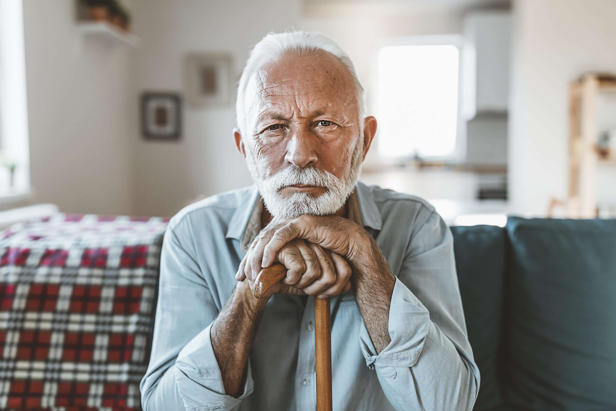 Elderly man with cane sitting indoors