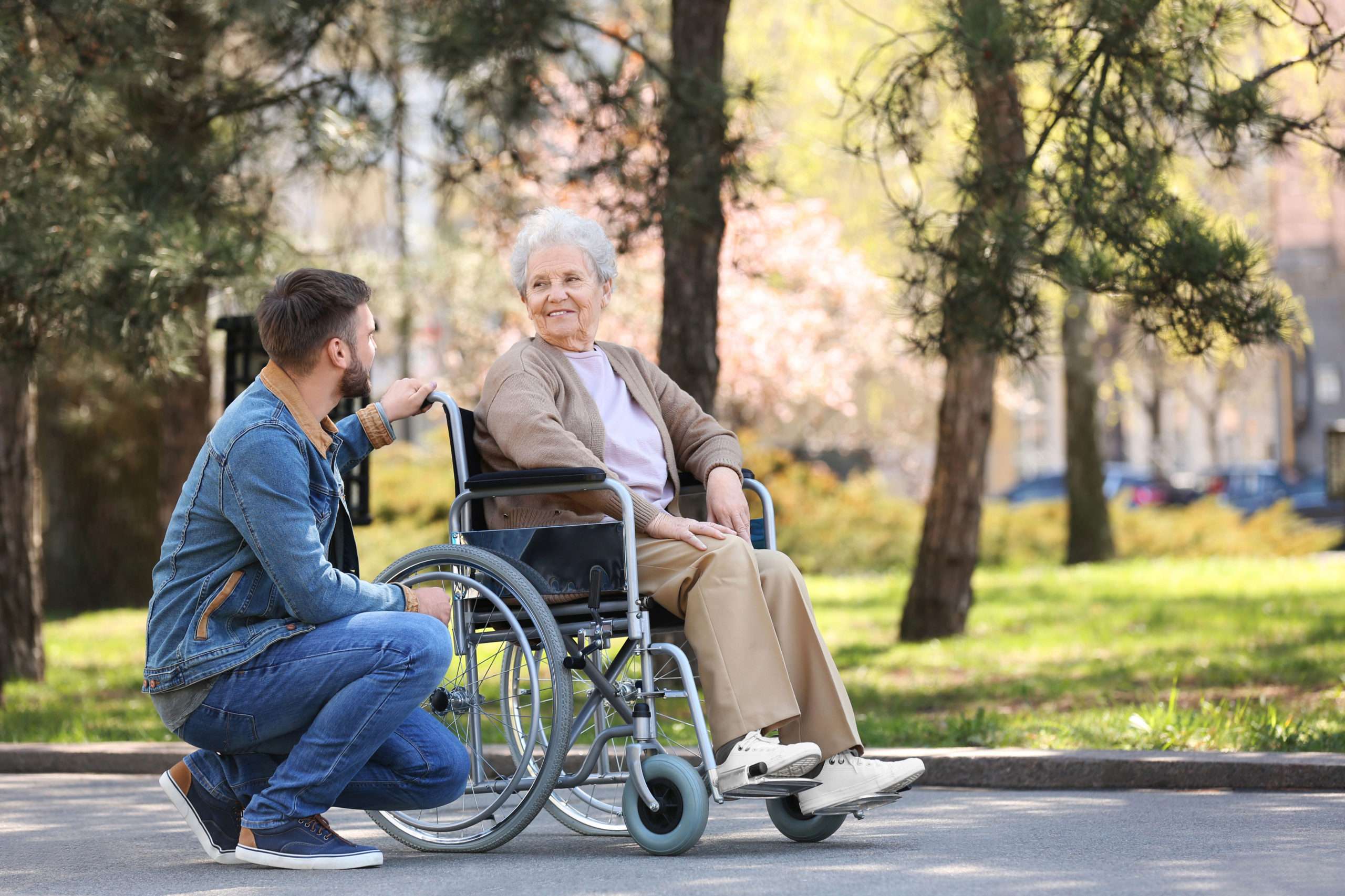 Senior woman in a wheelchair smiles outdoors with caregiver.