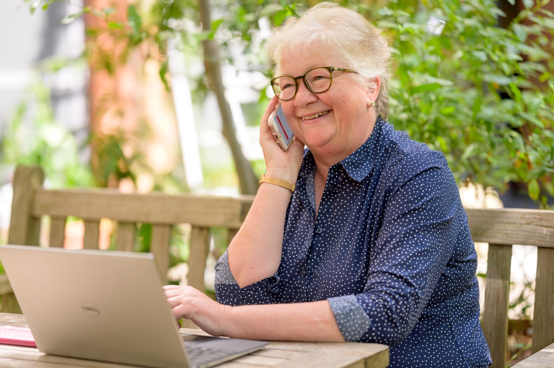 Senior woman using a laptop outdoors on a bench.