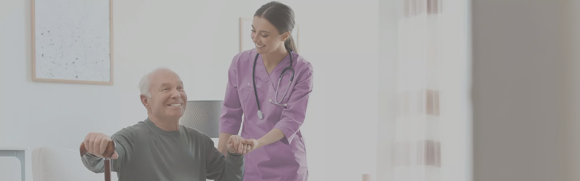 Caregiver assisting a smiling elderly man in a cozy room.