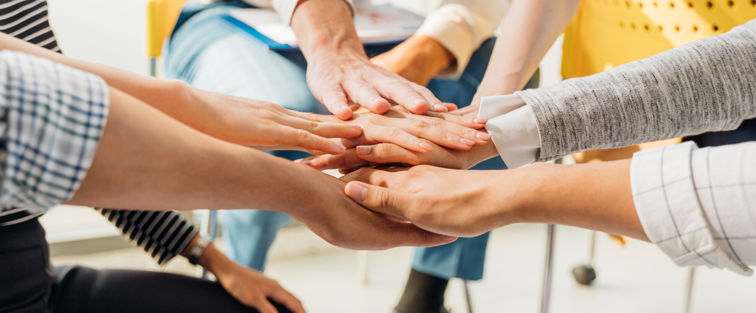 Multiple hands joining together in a supportive gesture.