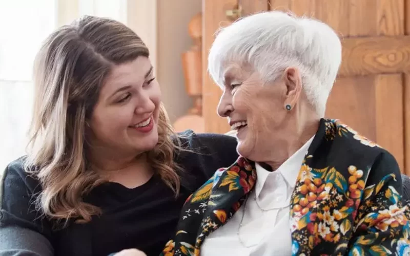 Smiling woman with gray hair and a caregiver.