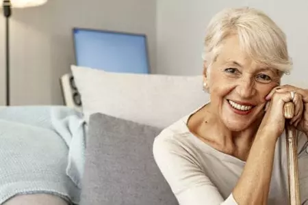 Smiling elderly woman with a cane in a cozy setting.