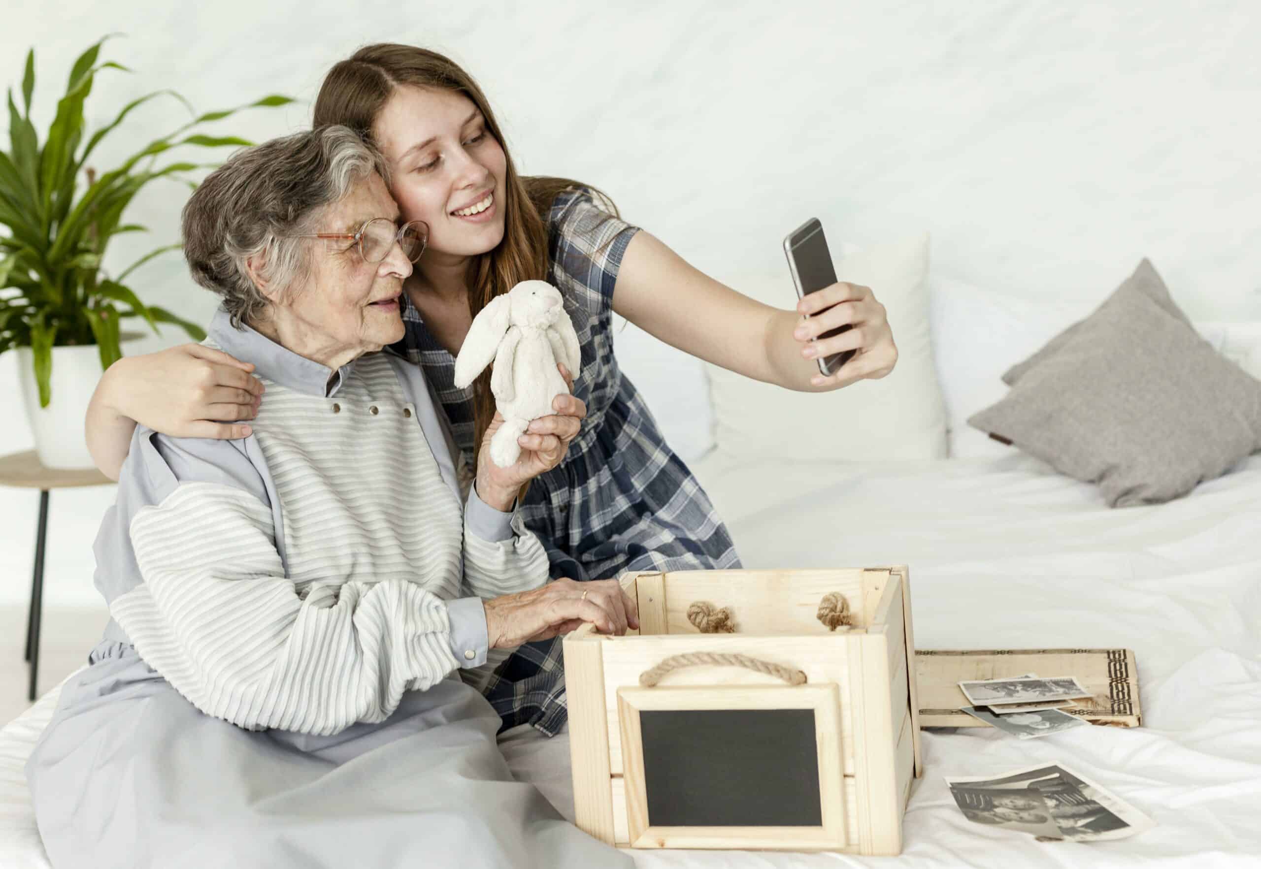 An elderly woman and a young woman taking a selfie in a bedroom.