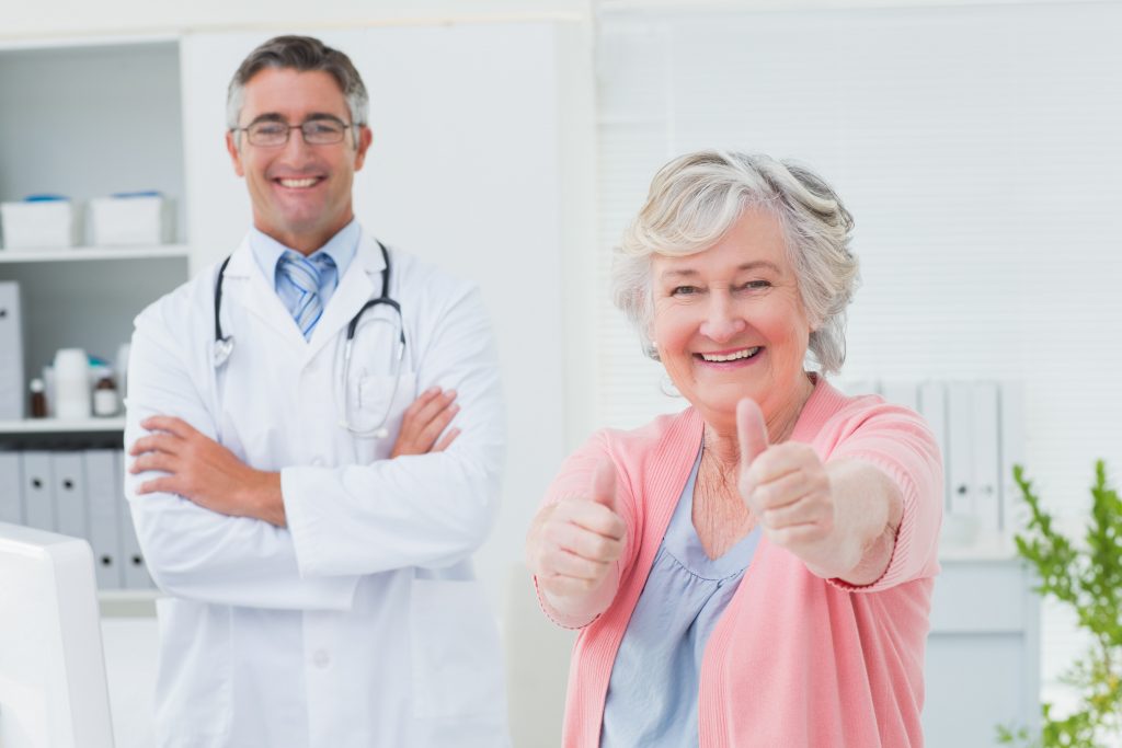 A smiling senior woman giving a thumbs up with a doctor.