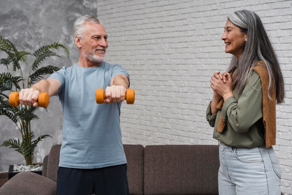 Senior man exercising with dumbbells, woman encouraging him