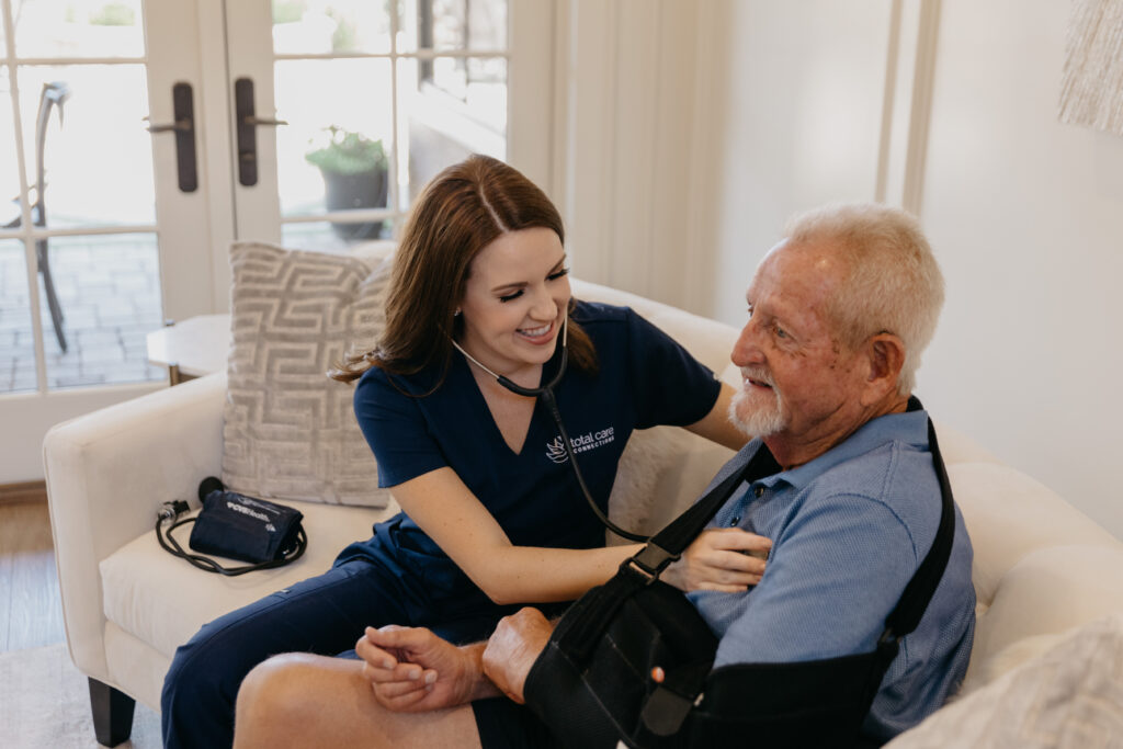 Healthcare worker assisting a senior man in a living room.