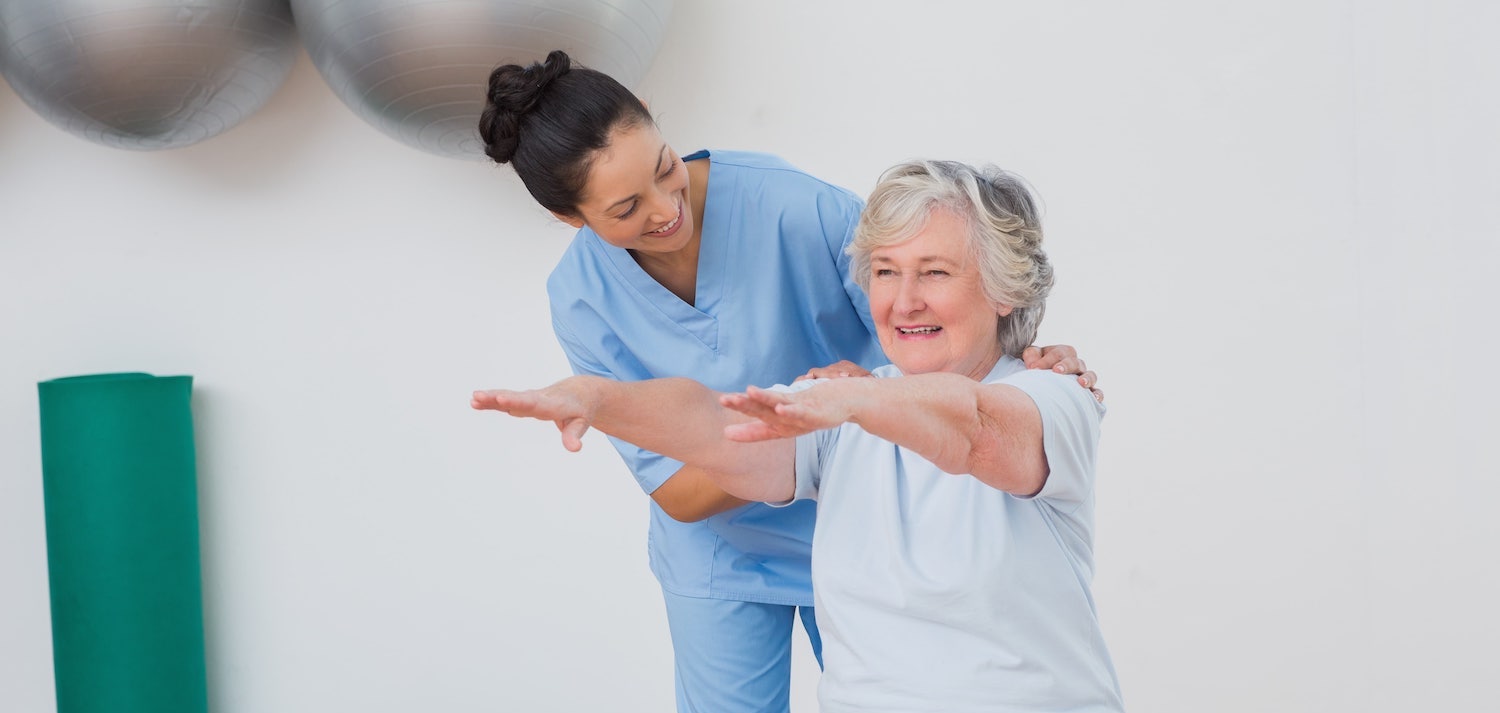 Elderly woman exercising with a caregiver's support.