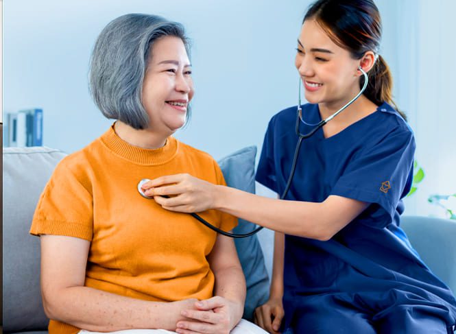 A nurse checks a resident's heartbeat on a couch.