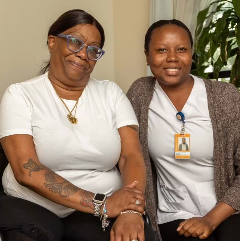 Two staff members smiling together in a bright room.