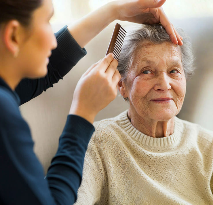 Caregiver styling the hair of an elderly woman