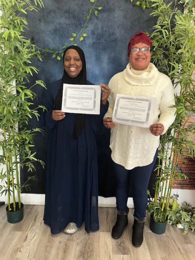 Two women holding certificates in a decorated space.