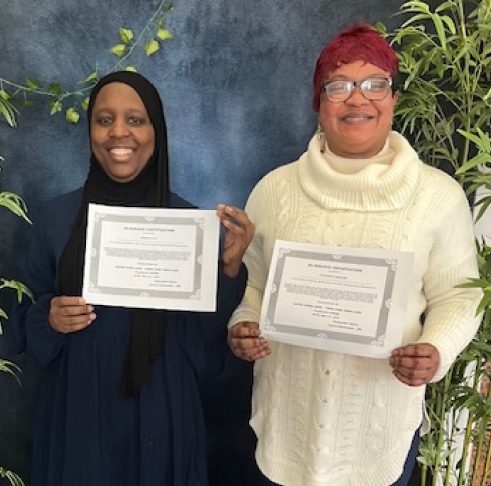 Two women holding certificates in a decorated space.
