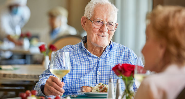 Elderly man enjoying a meal with a glass of wine.