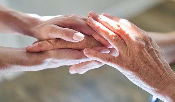 Hands of a caregiver and a senior holding each other