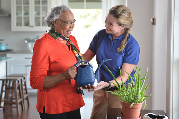 Staff assisting a resident with a watering can indoors.