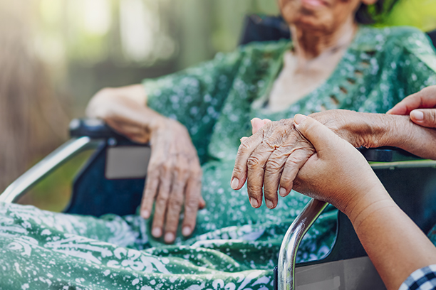 Elderly woman holding hands in a garden setting.