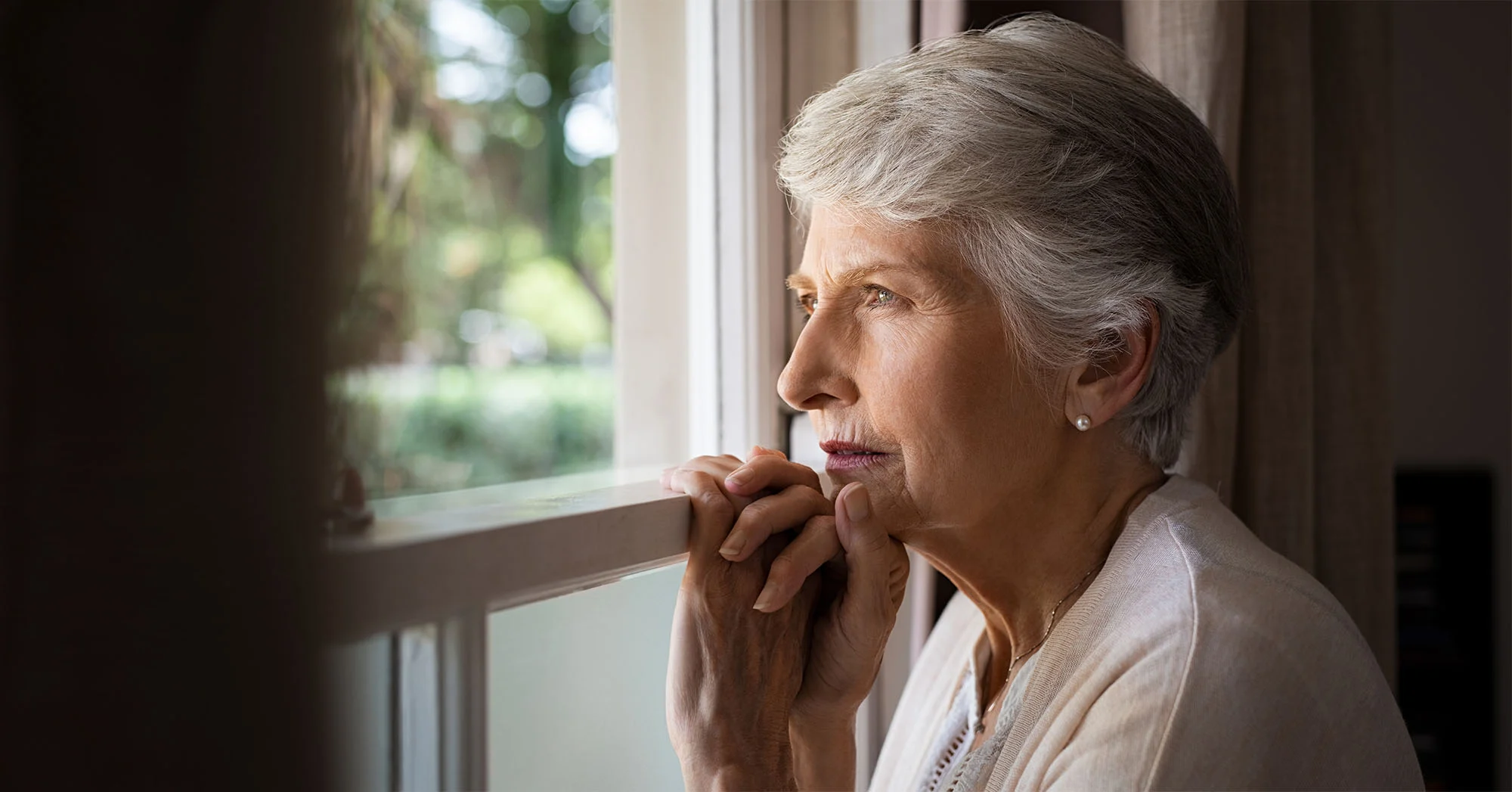 Senior woman looking thoughtfully out a window.
