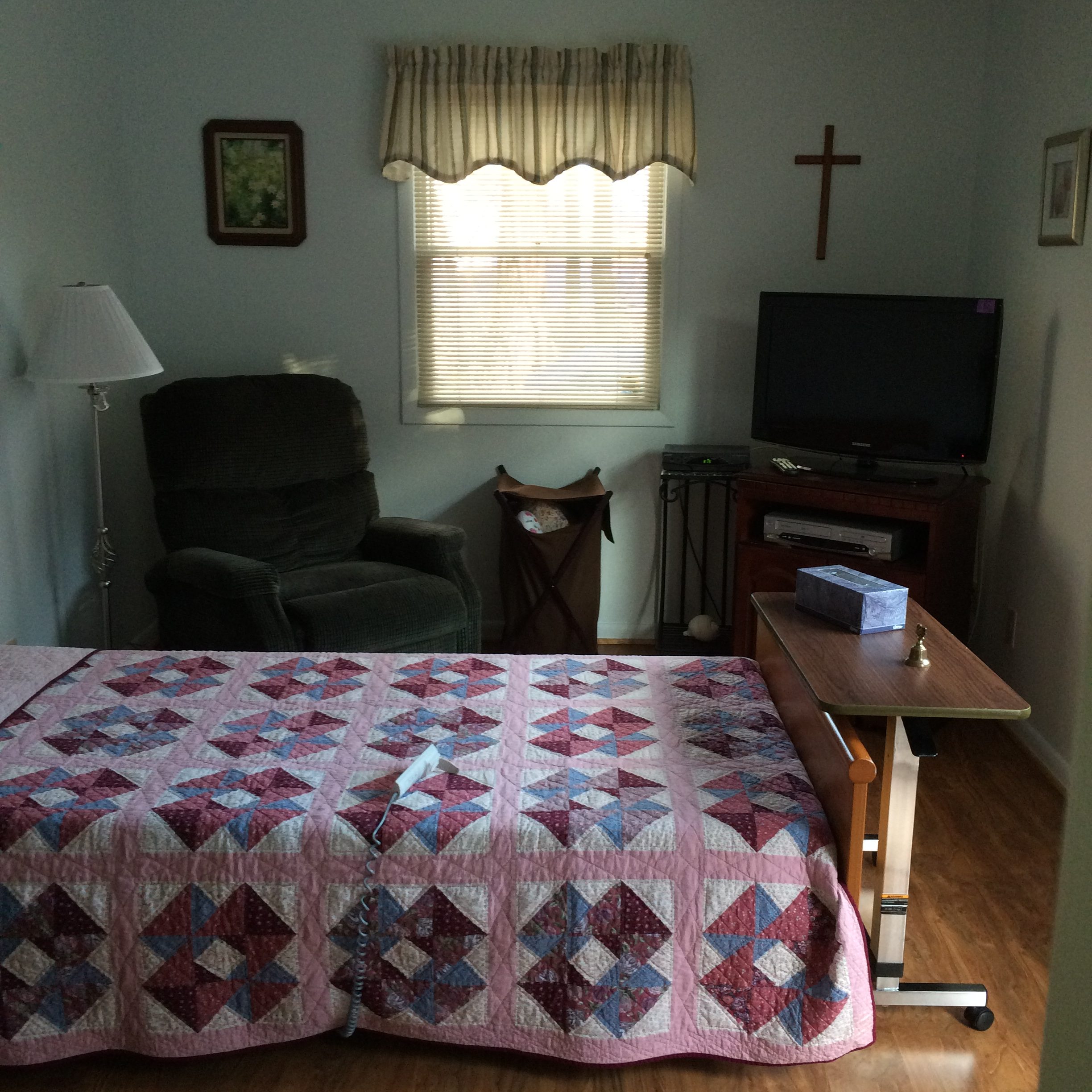 Cozy resident room with a quilted bed and chair.