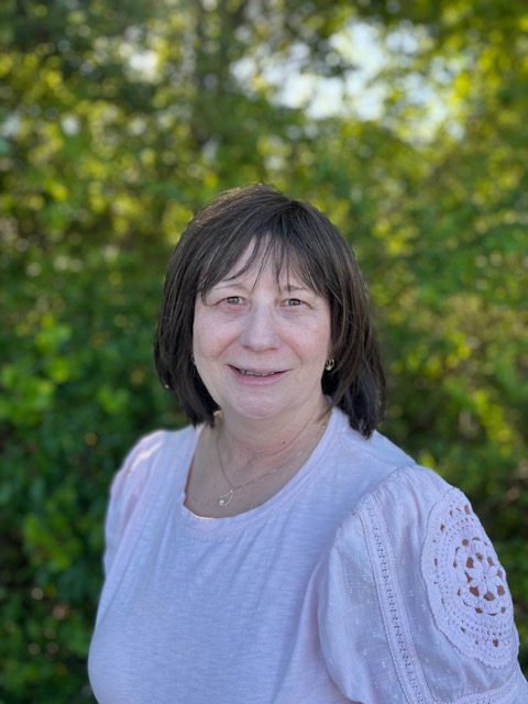Woman smiling outdoors among greenery.