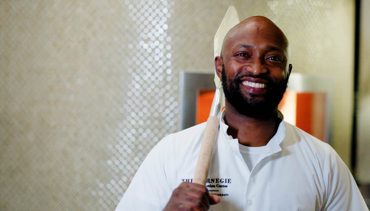 Chef smiling with a large cooking utensil in a kitchen