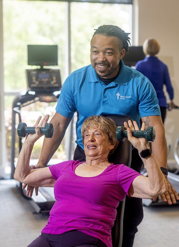 Trainer assisting a resident with weights in the fitness area