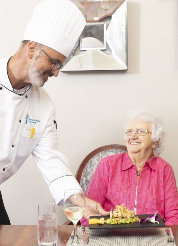 Chef serving a meal to a smiling elderly woman