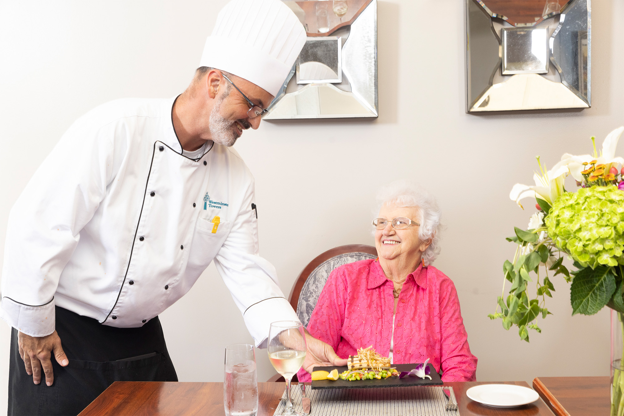 Chef serving food to a smiling resident in a dining room