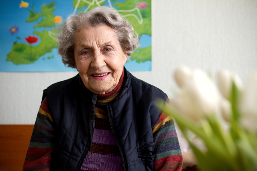 Smiling elderly woman sitting indoors with flowers