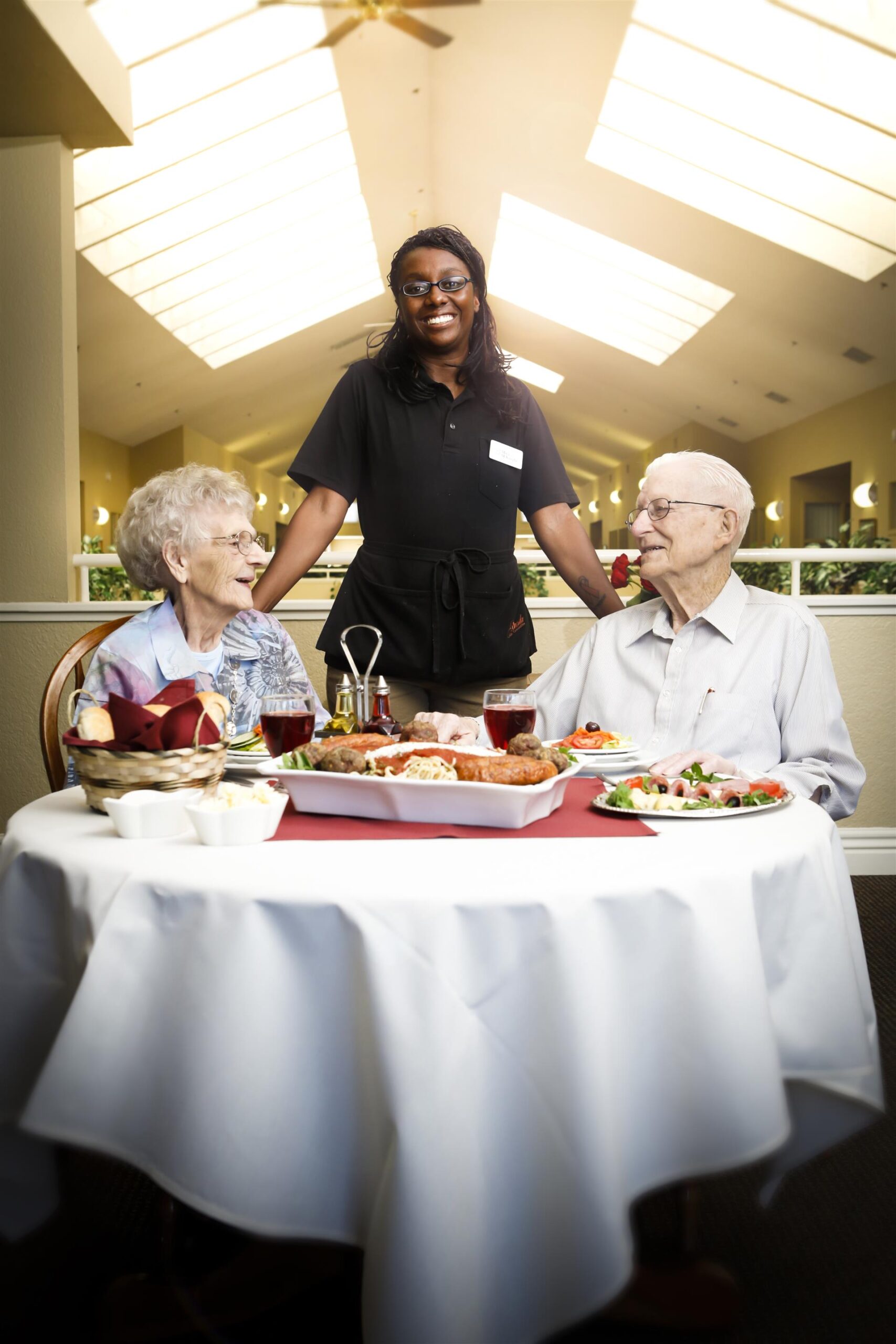 A staff member serving dinner to two residents in a dining area