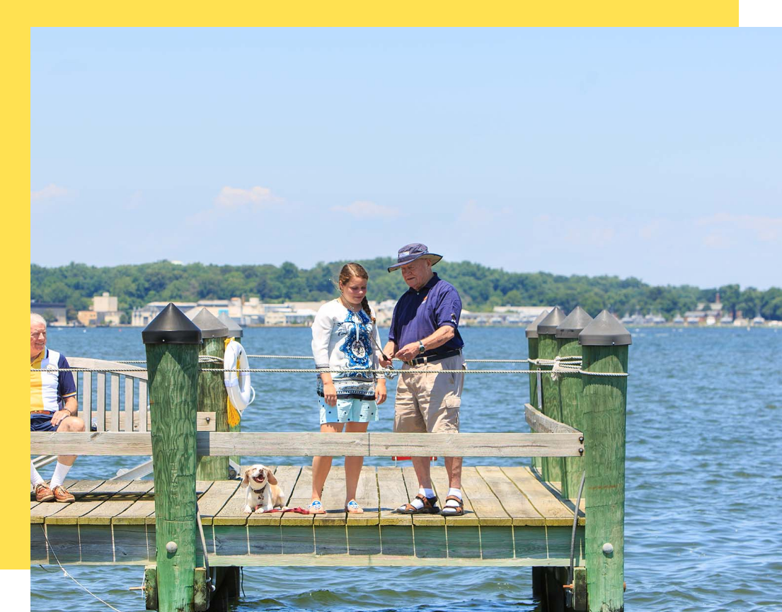 A senior man fishing with a young girl on a dock