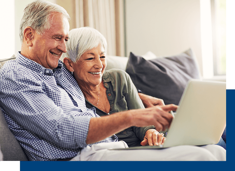 An elderly couple happily using a laptop together on a couch