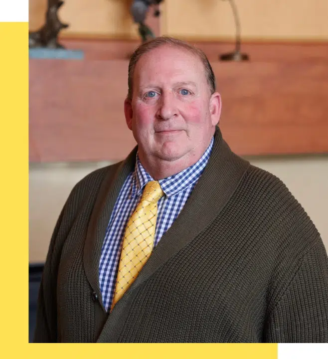 A man in a cozy sweater with a yellow tie.