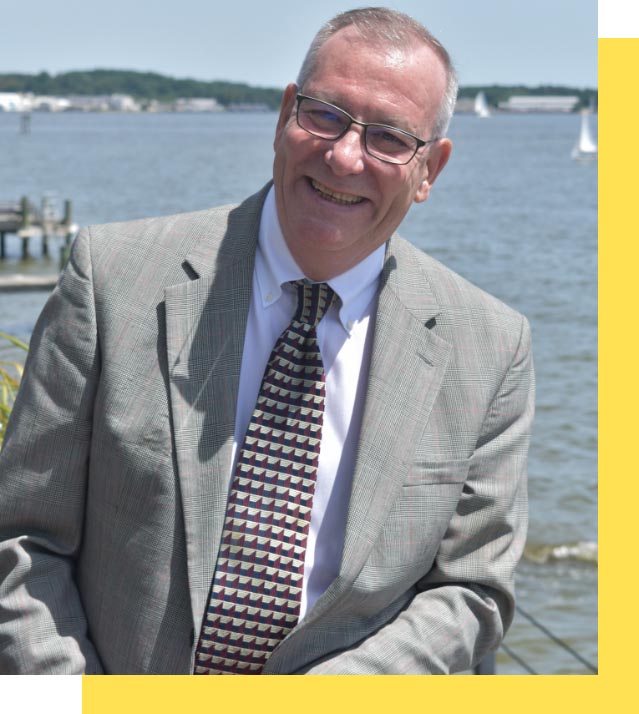 Man smiling by the water with boats in the background