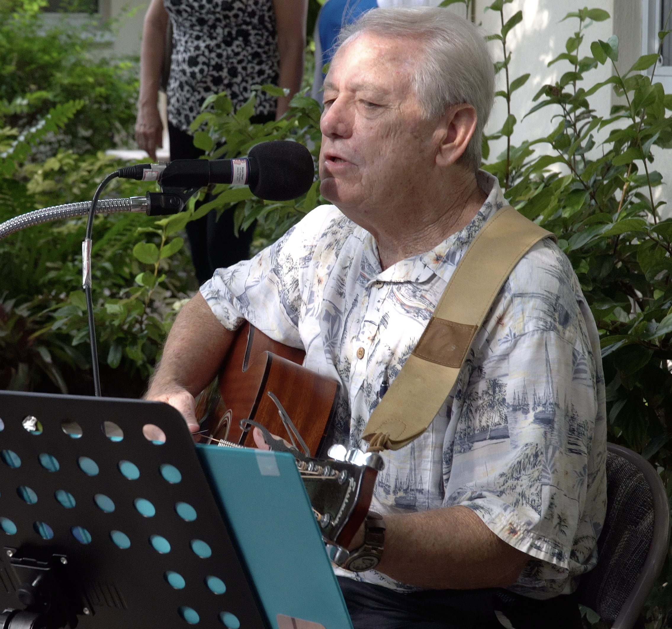 Senior resident playing guitar in a garden area.