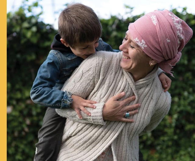 Woman with a pink scarf carrying a boy on her back.
