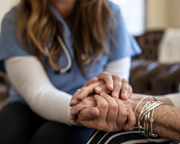 A nurse gently holding a resident's hands.
