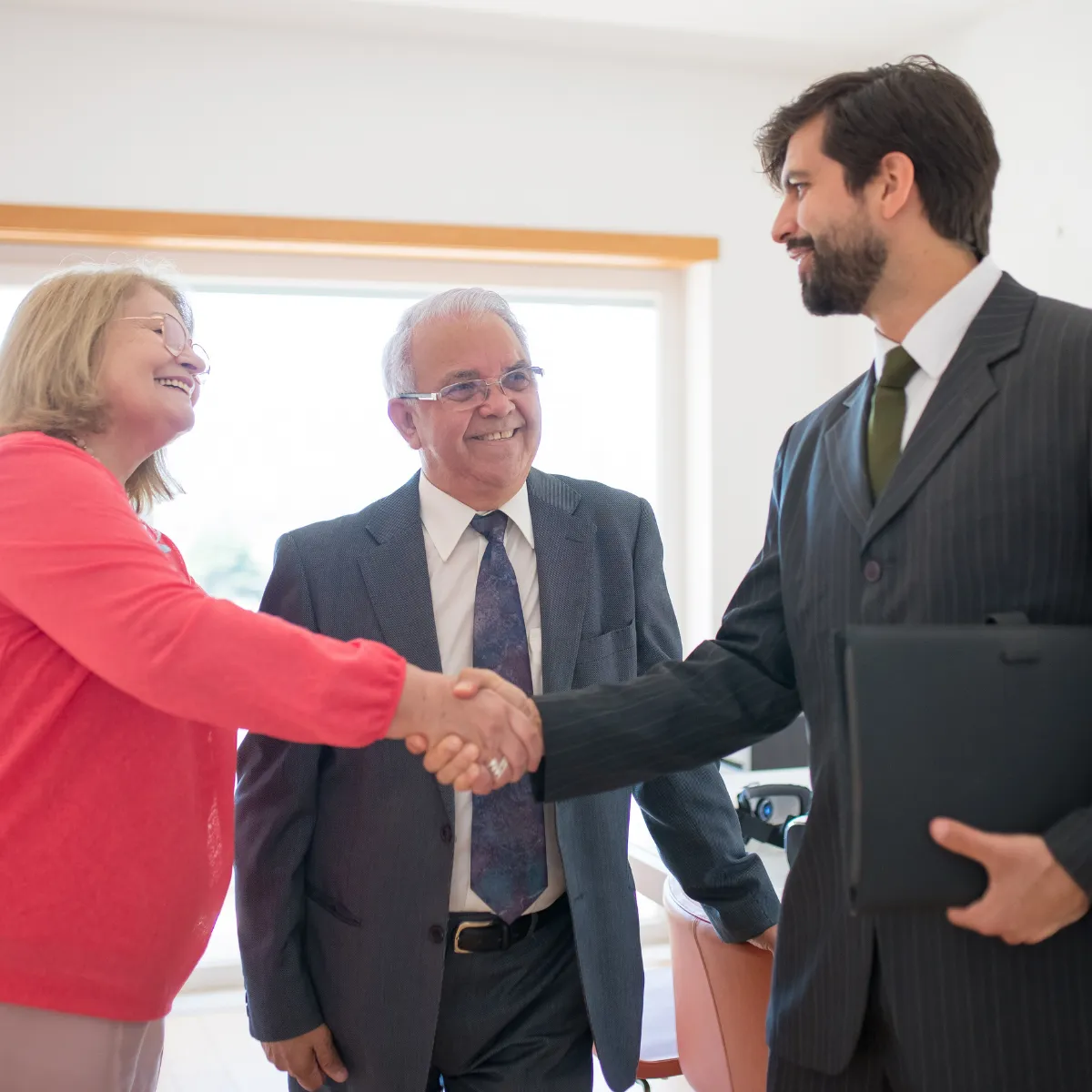Two seniors and a staff member shaking hands indoors.