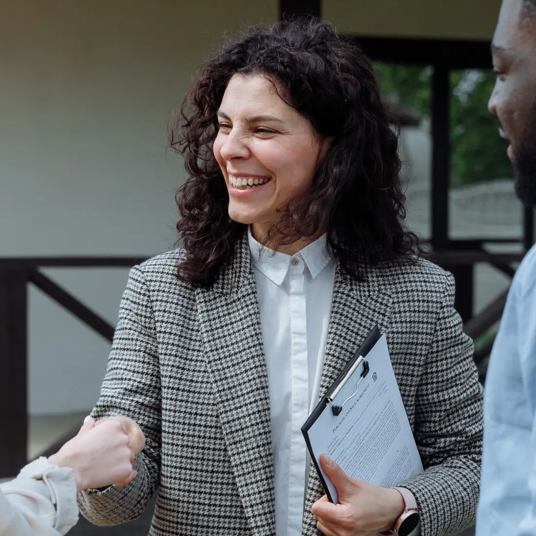 A woman smiling during a handshake outdoors.
