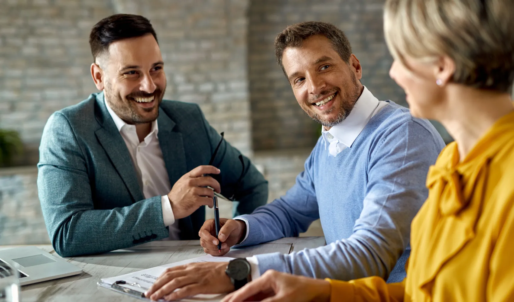 Three smiling individuals in a meeting setting.
