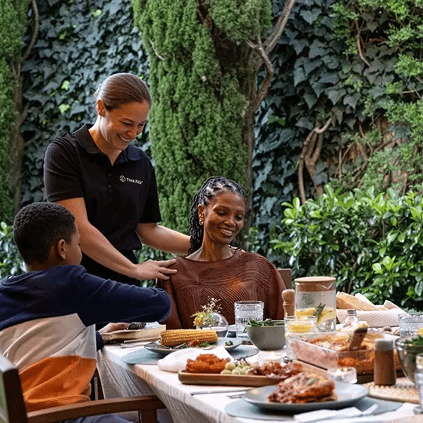 A caregiver assisting a resident at a meal outdoors.