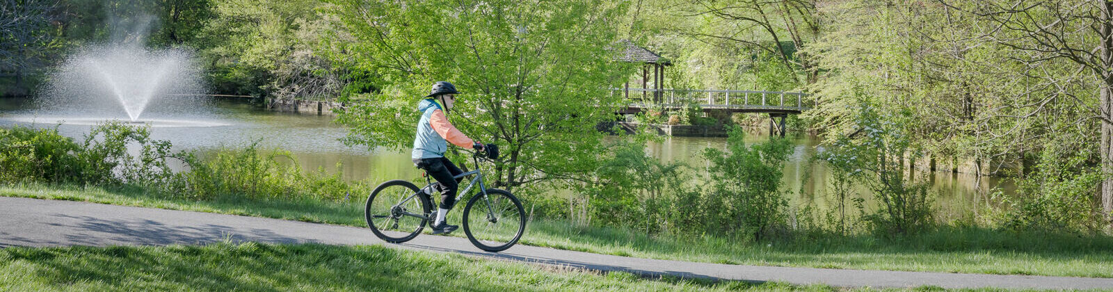A person biking near a pond with greenery
