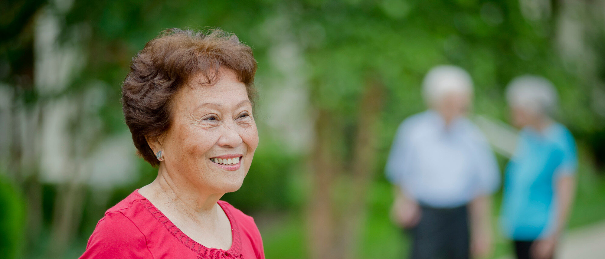 Senior woman smiling outdoors with blurred background.