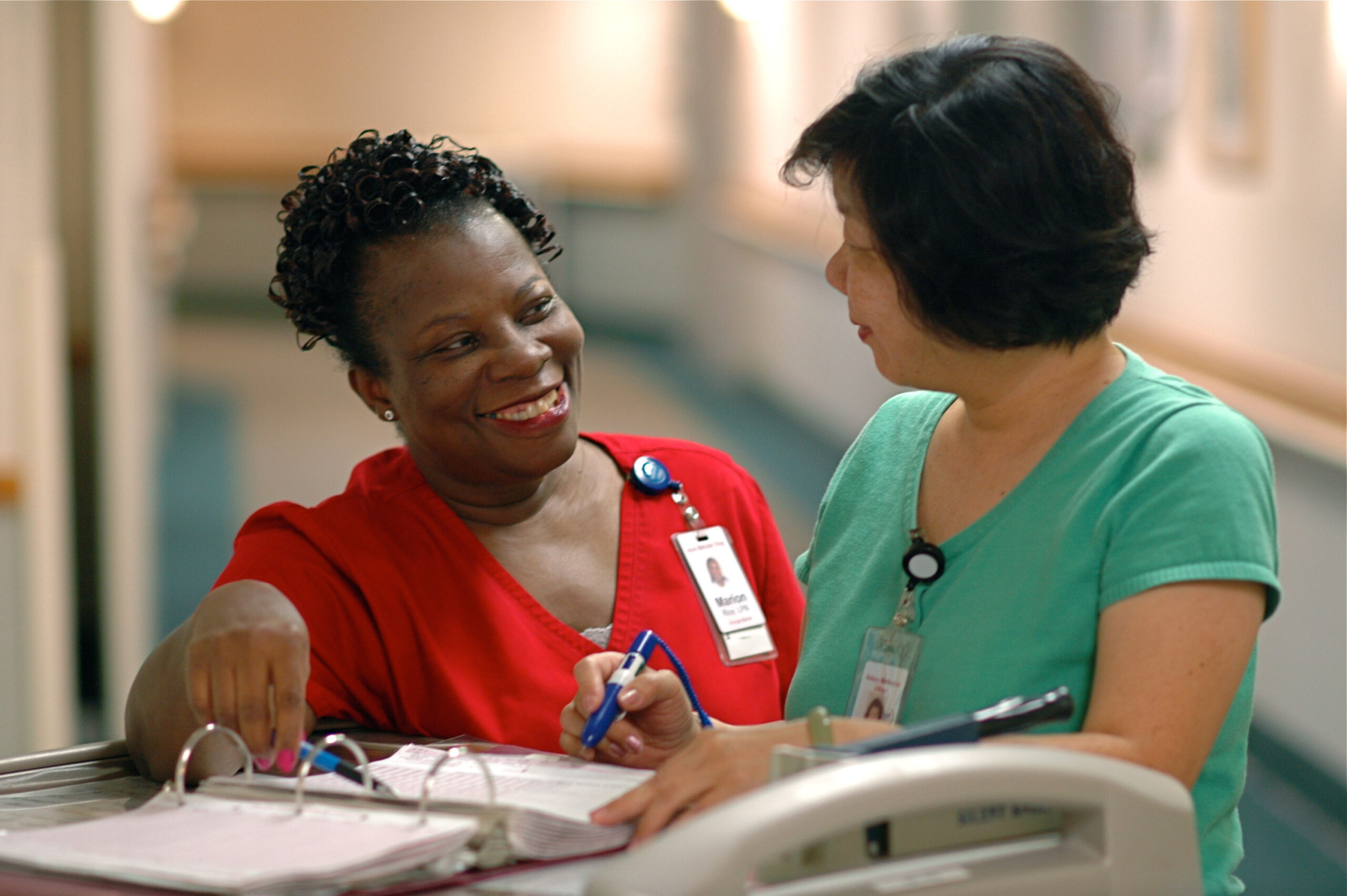 Two caregivers smiling and interacting in a hallway