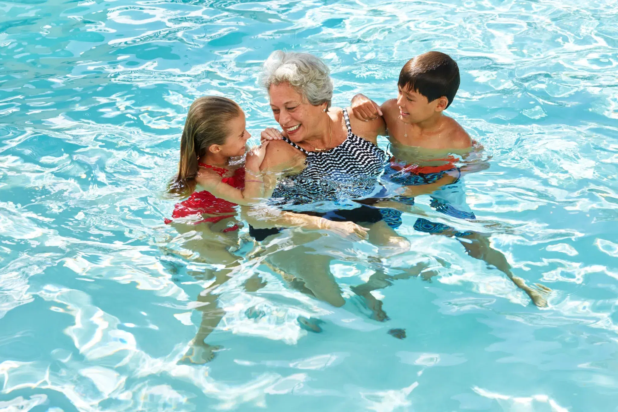 An elderly woman swimming with two children in a pool