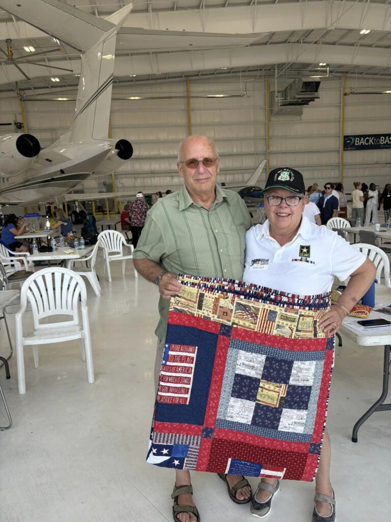 Two residents showcasing a handmade quilt in a community space