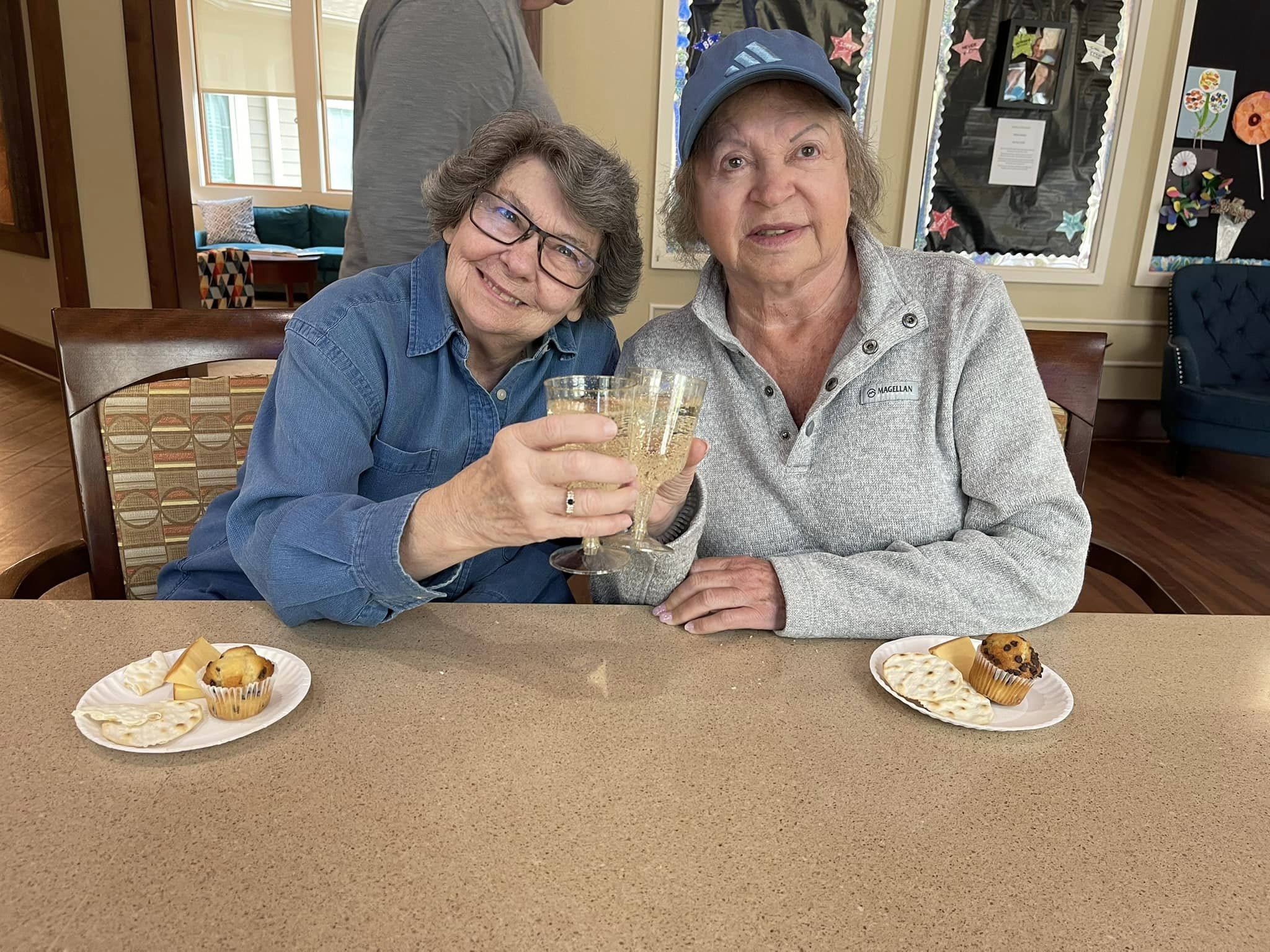 Two women toasting with drinks at a table.