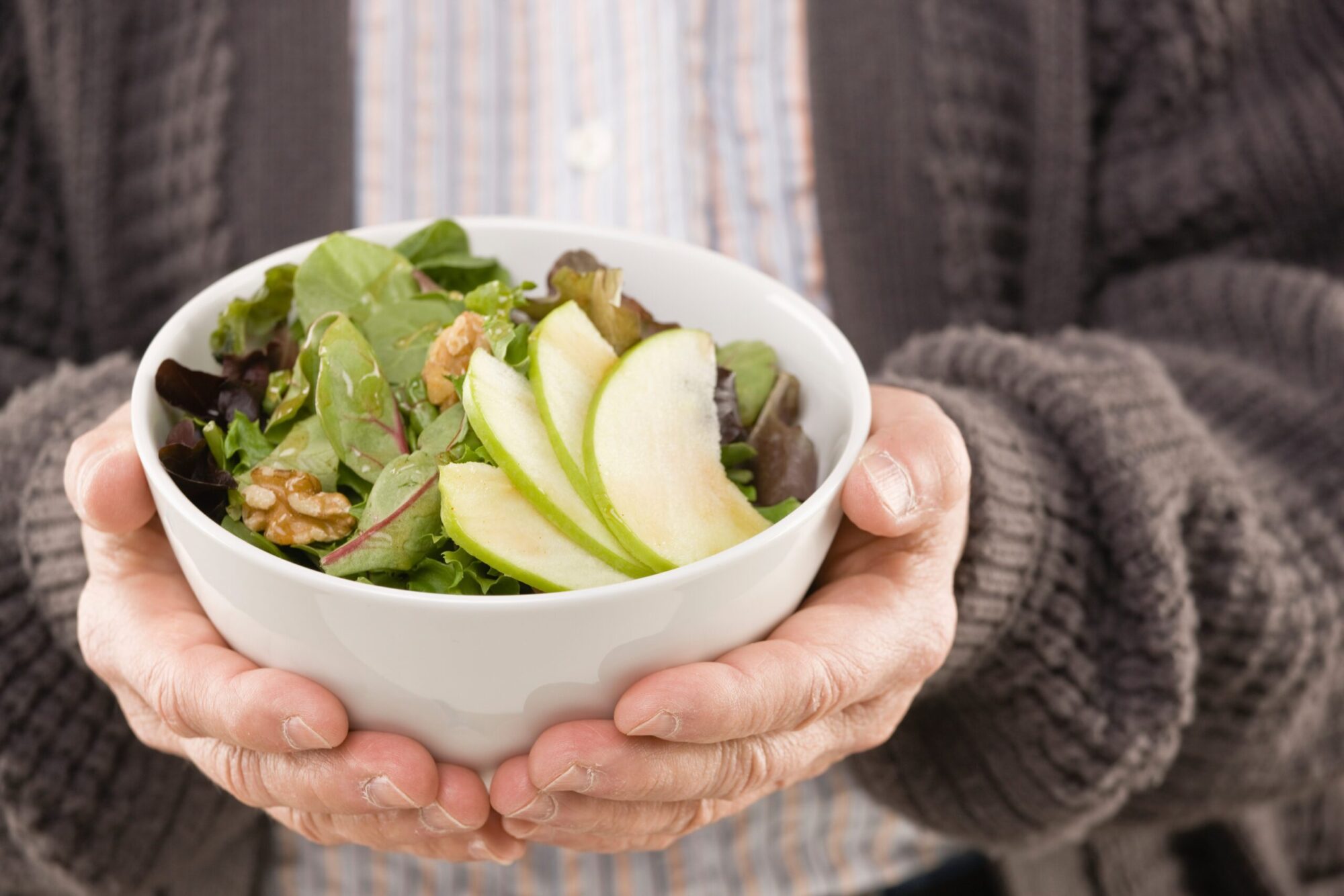 An elderly person holding a bowl of salad.