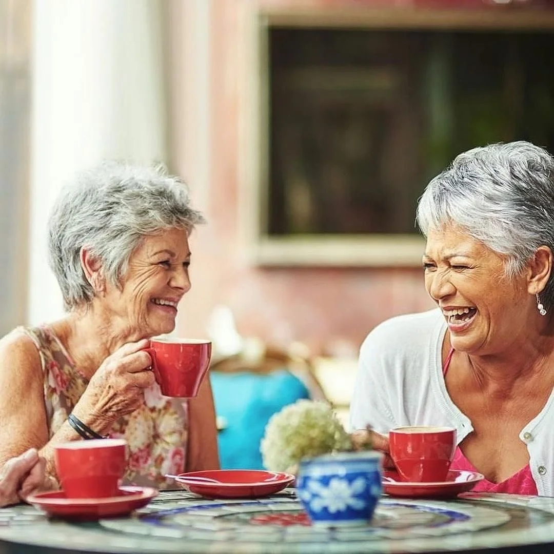 Two senior women enjoying coffee together and laughing.
