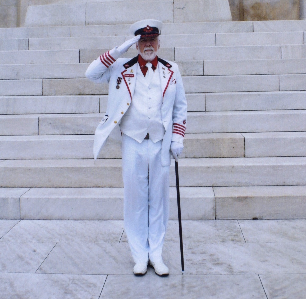 A man in a white uniform saluting on stone steps.